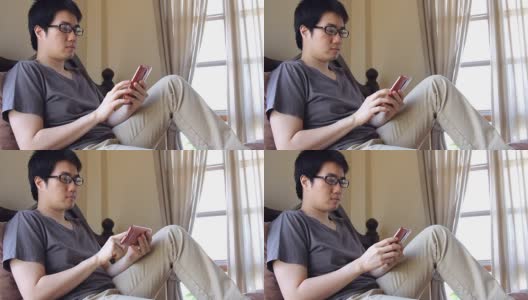 一名亚洲男子戴着眼镜在床上用手机发短信高清在线视频素材下载