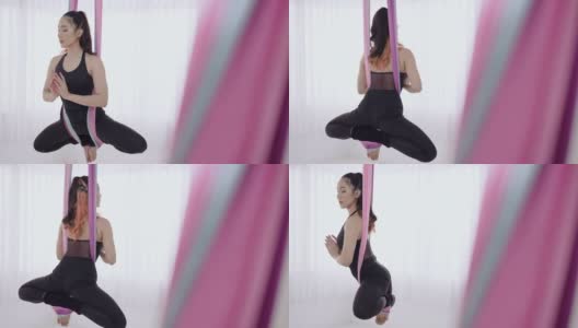 活跃的运动年轻的亚洲妇女在丝绸瑜伽吊床上做空中练习莲花姿势。柔韧性和专注力，反重力放松健身理念。漂亮年轻的亚洲妇女在黑色运动服做瑜伽的姿势。高清在线视频素材下载