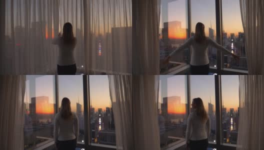 特写:兴高采烈的女人打开窗帘，看着夕阳下的城市。高清在线视频素材下载