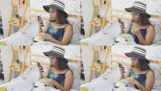 Beautiful young Asian women touching smart phone tablet on bed and eating pop corn高清在线视频素材下载