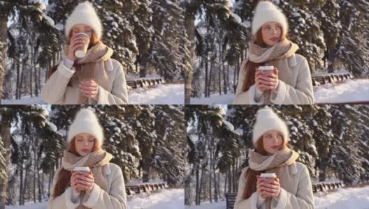 漂亮的年轻女子的肖像在温暖的衣服喝热咖啡从户外的杯子在阳光明媚的冬日。高清在线视频素材下载