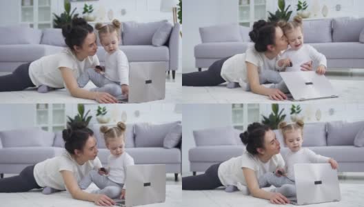 迷人的肖像，快乐的微笑灿烂的母亲，与她的可爱有趣的小女儿在地板上笔记本电脑高清在线视频素材下载