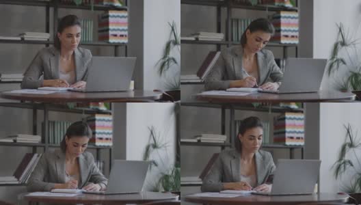 女商人在笔记本上写东西。创业女企业家学生在工作场所靠近电脑的地方学习写笔记。一位女士在桌上的空白笔记本上手写着什么。高清在线视频素材下载