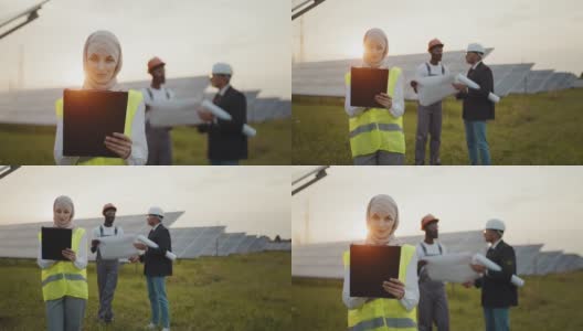 戴头巾的妇女在太阳能电站工作。戴着头巾的妇女站在太阳能电池板上看着相机。技术员和印度工程师进行背景讨论高清在线视频素材下载