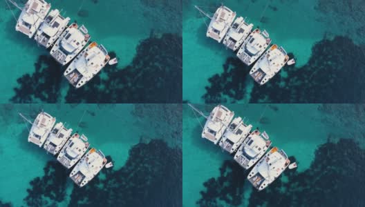 四艘游艇停泊在清澈的蓝绿色海水中，人们在船上工作。高清在线视频素材下载