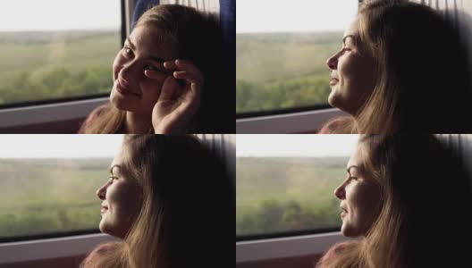 迷人的年轻女孩正对着镜头微笑。乘火车旅行。窗外的绿色自然。女孩若有所思地看着窗外。近距离高清在线视频素材下载