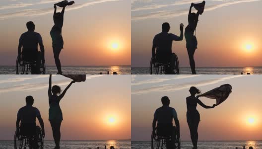 长腿女人站在防波堤上，挥舞着一块布，在一个跛脚到轮椅上的男人面前，背景是河上橙色的日落高清在线视频素材下载