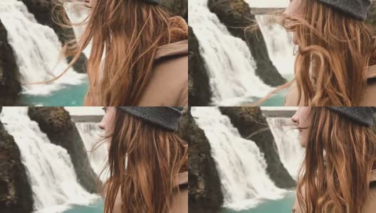 近距离观看年轻女子站在冰岛一个强大的瀑布附近，头发随风摆动高清在线视频素材下载