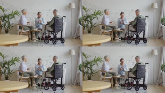 一组三个老人，两个坐在轮椅上的老年妇女和残疾老人，在养老院的公共休息室打牌，宽镜头高清在线视频素材下载