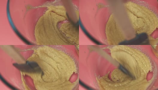 在粉色桌子上的一个玻璃碗里，用4K搅拌融化的红糖。用红糖搅拌面团制作巧克力曲奇饼干的概念。高清在线视频素材下载