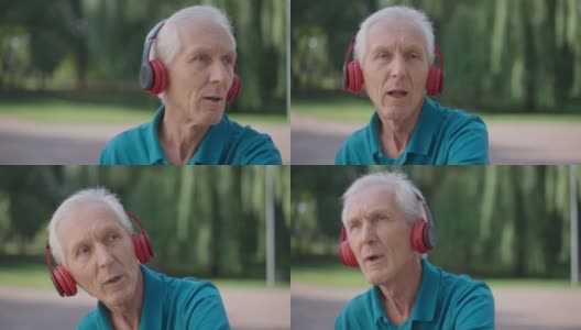 无忧无虑的白人老人的特写照片，慢动作唱歌跳舞，戴着耳机听着音乐。放松的退休男性享受爱好户外在夏季春天公园。爱好生活方式。高清在线视频素材下载