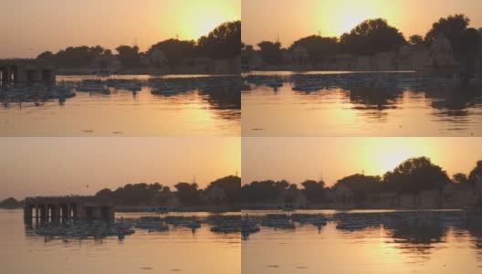 在印度拉贾斯坦邦Jaisalmer的加迪萨尔湖，日落时分，恰特里站在湖中央。日落时，恰特里亭在橘黄色湖水中的倒影。高清在线视频素材下载