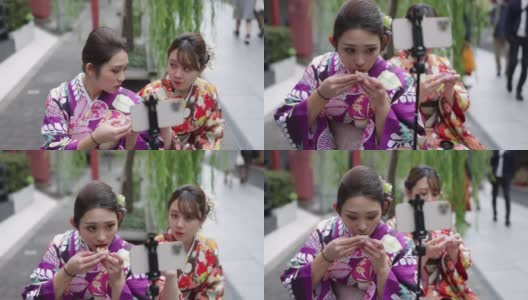 穿着和服的年轻女性朋友为了拍视频而吃街头小吃高清在线视频素材下载
