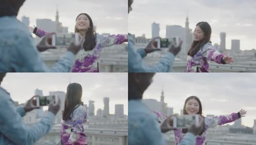快乐的年轻亚洲女人在屋顶上摆姿势与摄影师与智能手机高清在线视频素材下载