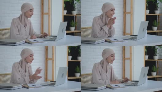 一位亲切微笑的穆斯林妇女正在手提电脑上上网，与同事进行电话会议。一位戴着头巾的美丽阿拉伯女子在一个没有偏见的新世界里使用互联网高清在线视频素材下载