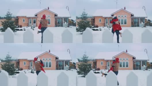 年轻美丽的夫妇跑出房子到院子里覆盖着新雪，他们旋转和跳舞。快乐的年轻人在神奇的冬天时间。高清在线视频素材下载