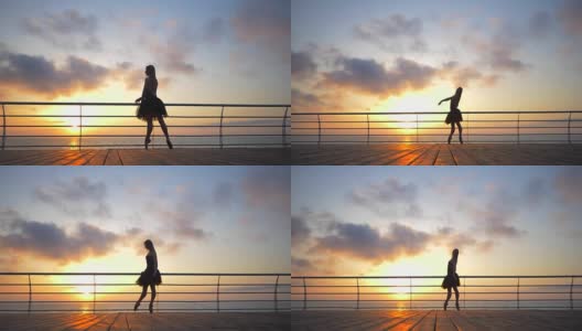 一个穿着黑色芭蕾舞裙的芭蕾舞女演员在日出或日落时在海洋或海滩的堤岸上跳着芭蕾舞。剪影的年轻美丽的金发女人长头发练习拉伸和练习。慢动作高清在线视频素材下载