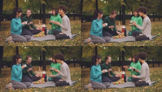 快乐的女孩们在公园里野餐，坐在瑜伽垫上，在秋天的户外练习后吃东西，女孩们有说有笑。沟通与美食理念。高清在线视频素材下载