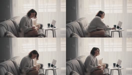 一个年轻的女人看着笔记本电脑的屏幕，在她的笔记本上做笔记高清在线视频素材下载