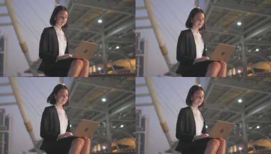 亚洲年轻美丽的商务女性工作和打字电脑坐在户外晚上在城市完成紧急工作。女孩在和朋友通过网络交流时感到快乐和微笑高清在线视频素材下载