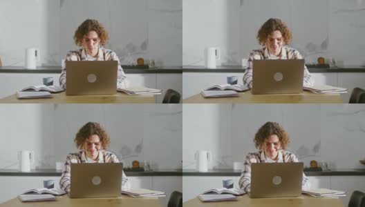 一个年轻人坐在书桌前用笔记本电脑，桌上放着许多书和笔记本高清在线视频素材下载