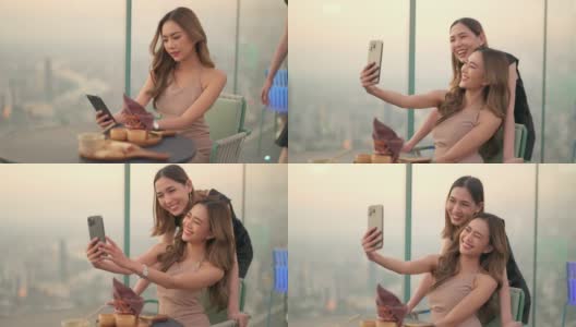日落时分，4K的亚洲女性朋友在摩天大楼的屋顶餐厅一起用智能手机自拍。高清在线视频素材下载