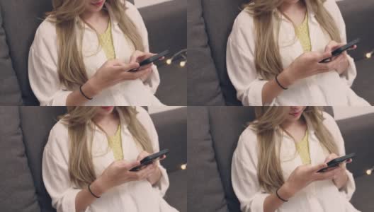 近景:穿着白衬衫的亚洲女性坐在沙发上，用智能手机在客厅浏览社交媒体。高清在线视频素材下载