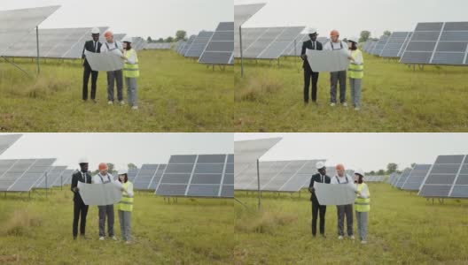 一群多民族的人戴着安全帽盯着太阳能农场，看着图纸。2名工程技术人员审核室外光伏建设方案。太阳能工厂工人高清在线视频素材下载