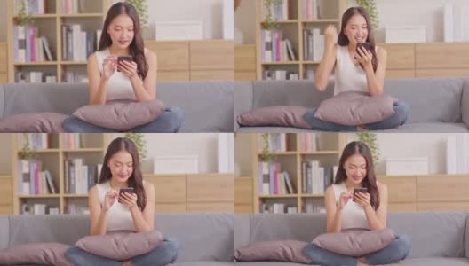 千禧一代的亚洲年轻女性看着手机笑着说着好消息或在家网上购物的折扣券。快乐而开朗的女人看着手机app读着短信感到兴奋高清在线视频素材下载