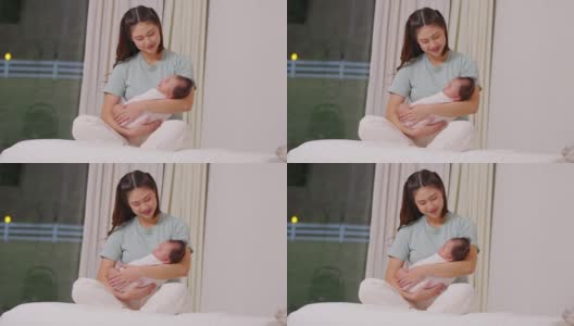 美丽的亚洲妈妈女人抱着新生的婴儿在她的手臂坐在床上白色舒适的家。宝宝开心宝宝笑在妈妈怀里安全舒适。母婴概念高清在线视频素材下载