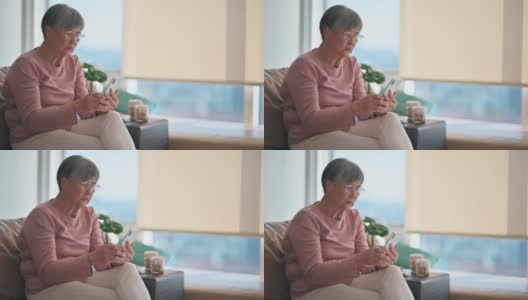 亚洲华人老年妇女使用智能手机阅读短信在她的公寓在城市高清在线视频素材下载