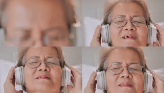 微笑的亚洲老年妇女坐在家里听音乐的肖像，防止。老年假期，技术，护理，人，退休，生活方式，医疗保健和医学，家庭概念。高清在线视频素材下载