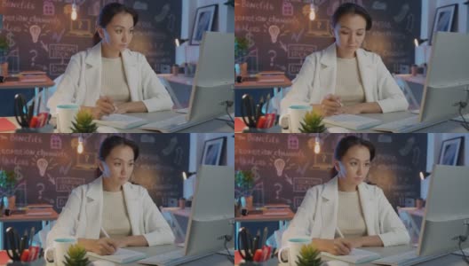 美丽的亚洲女商人记笔记看着电脑显示器工作在创造性的办公室在晚上高清在线视频素材下载
