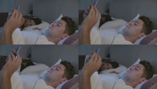 男人躺在床上看手机，而伴侣睡在他旁边高清在线视频素材下载