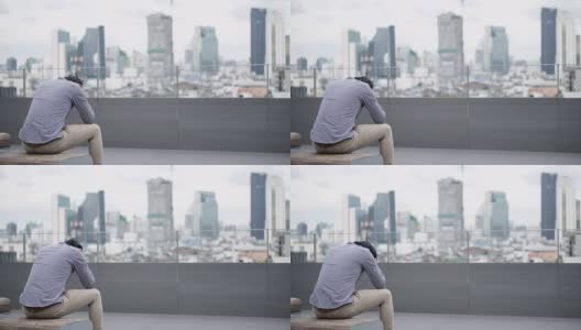 年轻的亚洲商人感到压力和沮丧的工作和生活问题坐在办公大楼屋顶露台的长凳上。背景中的城市视图。重度抑郁症的概念。高清在线视频素材下载