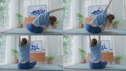 后视图:亚洲妇女伸展身体和瑜伽在客厅与宠物，看直播或视频电视在线教程。活动期间的隔离和社会距离的新常态概念。高清在线视频素材下载