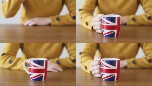 特写的手在一个木制的桌子上一个英国国旗杯热气腾腾的饮料，被一个年轻的女人举起高清在线视频素材下载