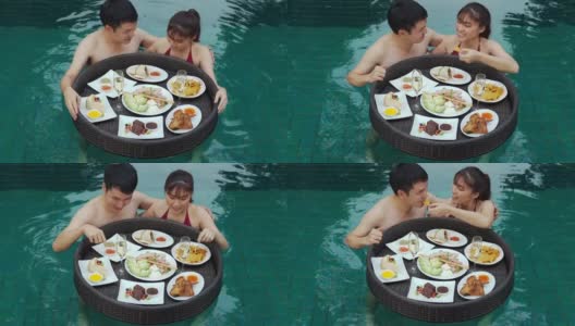 快乐的年轻夫妇享受和吃漂浮在游泳池的食物高清在线视频素材下载