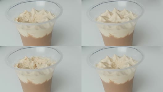 用塑料杯装掼奶油和巧克力的甜点。女性用茶匙将奶油顶部移除高清在线视频素材下载