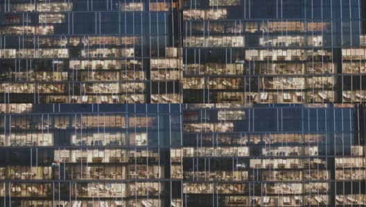 无人机拍摄的摩天大楼办公室在夜间的摄像头放大办公室的窗户，人们在他们的电脑上工作到很晚。高清在线视频素材下载