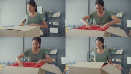 快乐美丽的亚洲女士打开纸箱从网上市场快递包裹在家里的客厅。高清在线视频素材下载