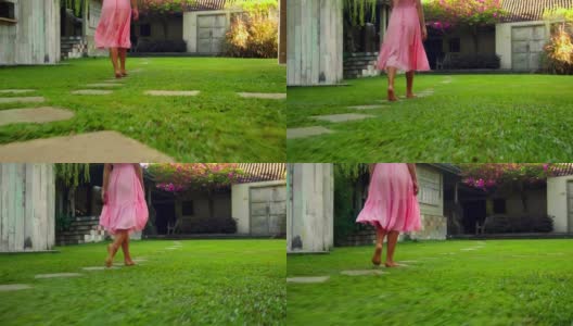 一个欧洲女孩走在有绿色花园和草地的后院，穿着漂亮的粉红色长裙，背过身去高清在线视频素材下载