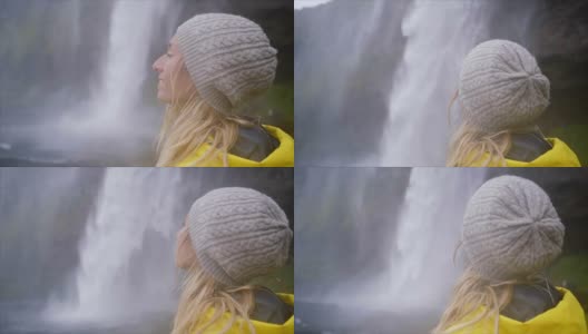 女游客在冰岛旅游的慢动作视频站在壮观的瀑布旁边，沉思着大自然，人们旅行冒险的概念高清在线视频素材下载