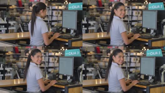 美丽的女收银员在电脑上工作，然后对着相机微笑在家具店高清在线视频素材下载