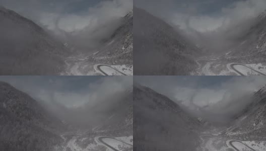 在一个高海拔的山谷里，一架无人机穿过云层降落，山谷下面有一条小路高清在线视频素材下载