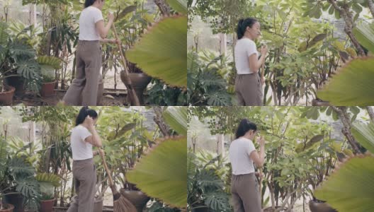 亚洲妇女在后院花园用扫帚扫干树叶家。4 k慢动作。高清在线视频素材下载