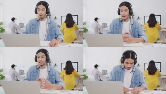 新常态下的亚洲商人社交距离为病毒预防在家庭办公室工作时使用笔记本电脑向同事介绍视频通话计划。高清在线视频素材下载