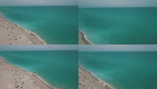 2021年3月春假和COVID-19期间，佛罗里达朱诺海滩正午沙滩上彩色沙滩伞和人们的动态鸟瞰图高清在线视频素材下载