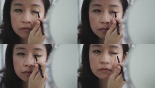 亚洲女人在镜子前化妆，画眼线的慢动作。美容化妆概念高清在线视频素材下载