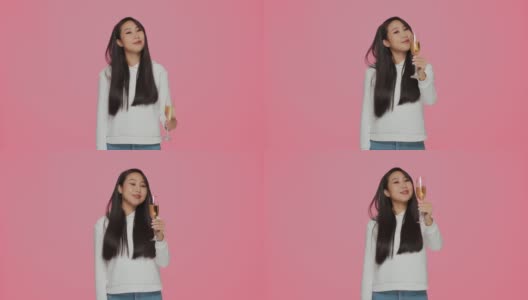 新年快乐。微笑的年轻亚洲女孩最好的祝愿喝香槟在粉红色的工作室背景。节日聚会高清在线视频素材下载